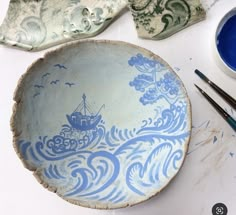 a blue and white bowl sitting on top of a table next to paintbrushes