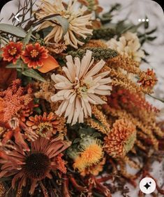 an arrangement of flowers and foliage on a white tablecloth with red, orange, yellow, and green leaves