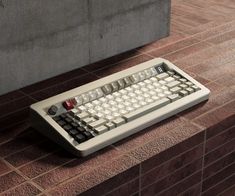 a computer keyboard sitting on the ground next to a brick wall and concrete block walls