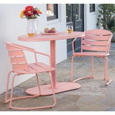 two pink chairs and a table with flowers on the side walk way in front of a house