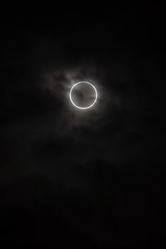 the moon is seen in the dark sky with clouds around it and an object that appears to be a solar eclipse