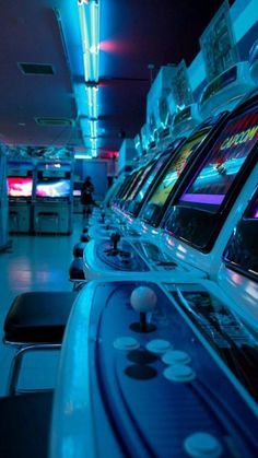 a row of video game machines in a room with blue lights and white tile flooring