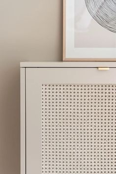 a close up of a white cabinet with an art piece on the wall behind it