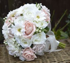 a bridal bouquet with pink and white flowers on a wicker tableclothed surface