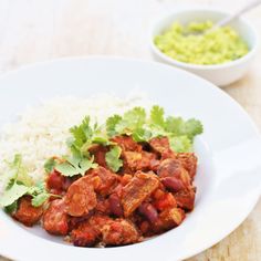 two white plates filled with meat and rice on top of a wooden table next to a bowl of guacamole