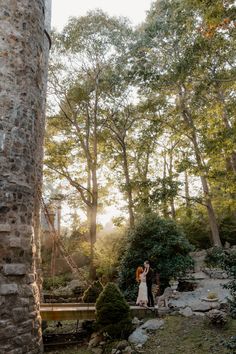 a bride and groom are standing in the woods near a stone structure with trees around them