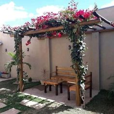 a wooden bench sitting under a pergoline covered arbor with red flowers on it