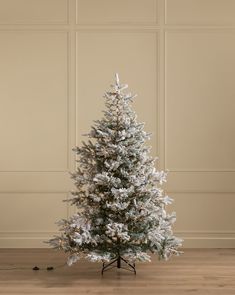 a white christmas tree with snow on the branches and lights in front of a beige wall