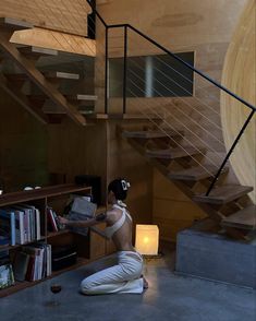 a woman sitting on the floor in front of a book shelf next to a stair case