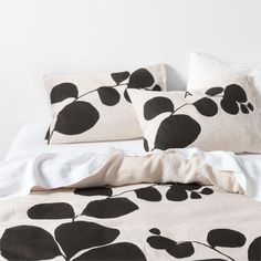 a bed with black and white leaves on the pillowcase, along with two pillows