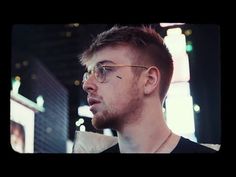 a man with glasses is looking off to the side in front of a neon sign