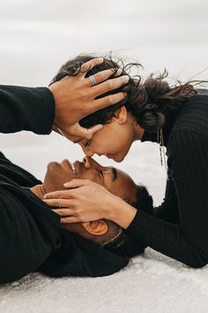 a man and woman laying on the ground kissing each other with their hands touching foreheads