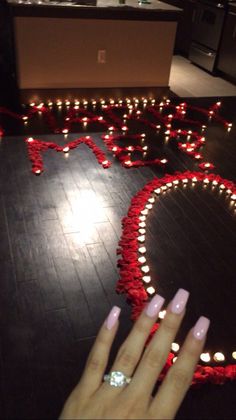 a woman's hand with pink nail polish on it next to a heart made out of candles