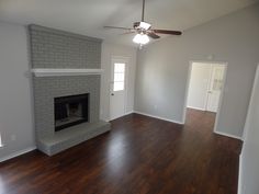 an empty living room with hard wood floors and a fireplace in the center, surrounded by white walls