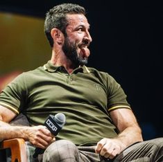 a man with a beard sitting in a chair and holding a microphone to his mouth