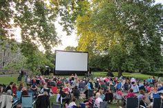 a large group of people sitting in lawn chairs watching a movie on a big screen