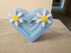 a blue heart shaped object with two flowers on it sitting on a bed next to a wall