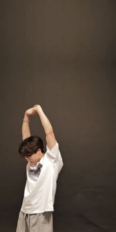 a young boy standing in front of a black background holding his arms up with both hands