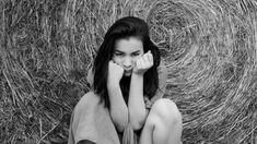 a woman sitting on the ground in front of hay bales with her hands to her face