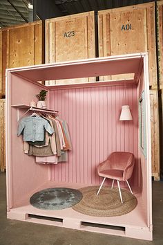 a pink closet with clothes hanging on hangers and a chair in front of it