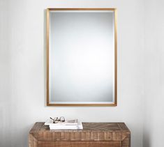 a mirror on the wall above a wooden table with books and glasses next to it