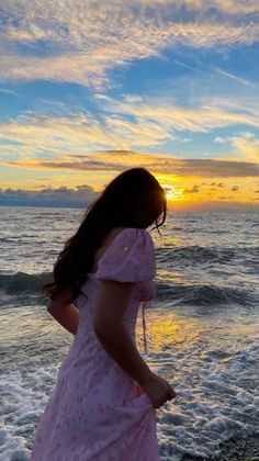 a woman standing on top of a sandy beach next to the ocean at sun set