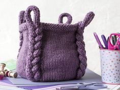 a knitted purse sitting on top of a table next to a cup with pens and pencils in it