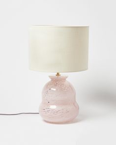 a pink glass lamp with a white shade on it's base and a cord plugged in