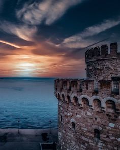 the sun is setting over an old brick tower by the water with clouds in the sky