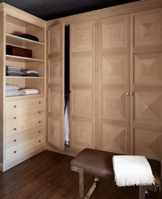 an empty bedroom with wooden closets and white sheets on the bed, along with a footstool