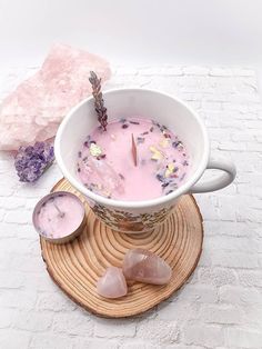 a white bowl filled with pink liquid next to two crystal rocks and a candle on top of a wooden coaster