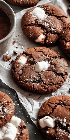 chocolate cookies with marshmallows and powdered sugar are on parchment paper next to a cup of coffee