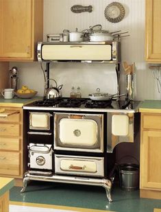 an old fashioned stove in the middle of a kitchen with wooden cabinets and green flooring