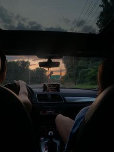 two people driving in the back seat of a car at sunset or dawn with their hands on the steering wheel