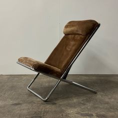 a brown leather chair sitting on top of a cement floor next to a white wall