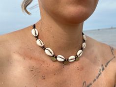 BOHO CHOKER NECKLACE with cowrie shells and brass pendants/beads and wooden elements. Surfer - boho jewelry. The length is adjustable with a slide closure. So you can wear the necklace as a choker close to your neck, or as a long necklace. You can also find a matching bracelet in the shop. Length adjustable from approx. 35 - 70cm Material: waxed macrame ribbon, cowrie shells, brass pendant, brass beads. You are very welcome to leave individual inquiries here or by e-mail. Casual Handmade Strand Shell Necklace, Casual Handmade Shell Necklace Strand, Handmade Casual Shell Necklace, Casual Handmade Shell Necklace For Festivals, Adjustable Beachy Necklace For Festivals, Casual Handmade Cowrie Shell Necklace, Beachy Cowrie Shell Necklace For Festivals, Casual Shell Strand Necklace For Festivals, Casual Strand Shell Necklace For Festivals