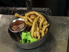 a bowl filled with fries and lettuce on top of a metal tray next to a dipping sauce