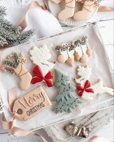 decorated christmas cookies in a gift box with ribbon and decorations on the table next to it