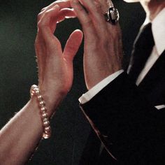 two people holding their hands up to each other while wearing pearls and rings on their fingers