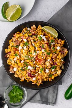 mexican street corn salad in a black bowl with limes and cilantro on the side