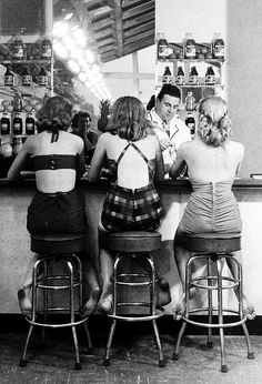 three women are sitting at the bar with their backs to each other and one woman is standing behind them