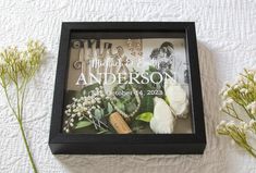 a black frame with flowers and pearls on it sitting next to a couple's wedding rings