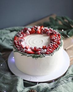 a white cake topped with strawberries on top of a wooden table next to pine cones