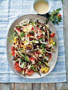 a white plate topped with salad next to a cup of coffee and spoons on a blue table cloth