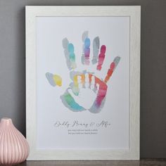 a hand print is displayed on a shelf next to a vase with a pink flower