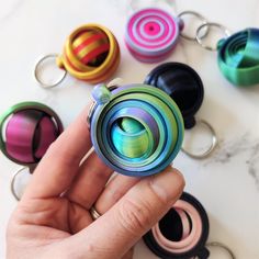 a hand holding a colorful metal object in front of many other colored objects on a table