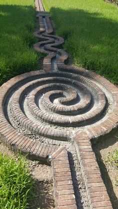 a brick pathway that is in the middle of some grass and has a spiral design on it