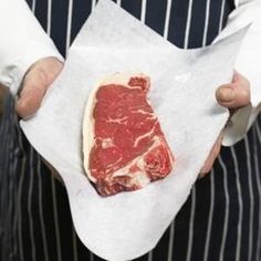 a man in an apron holding a piece of raw meat on top of white paper