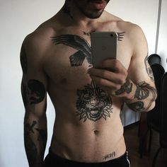 a man with tattoos on his chest holding a cell phone