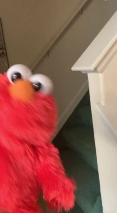 a red stuffed animal with big eyes standing next to stairs